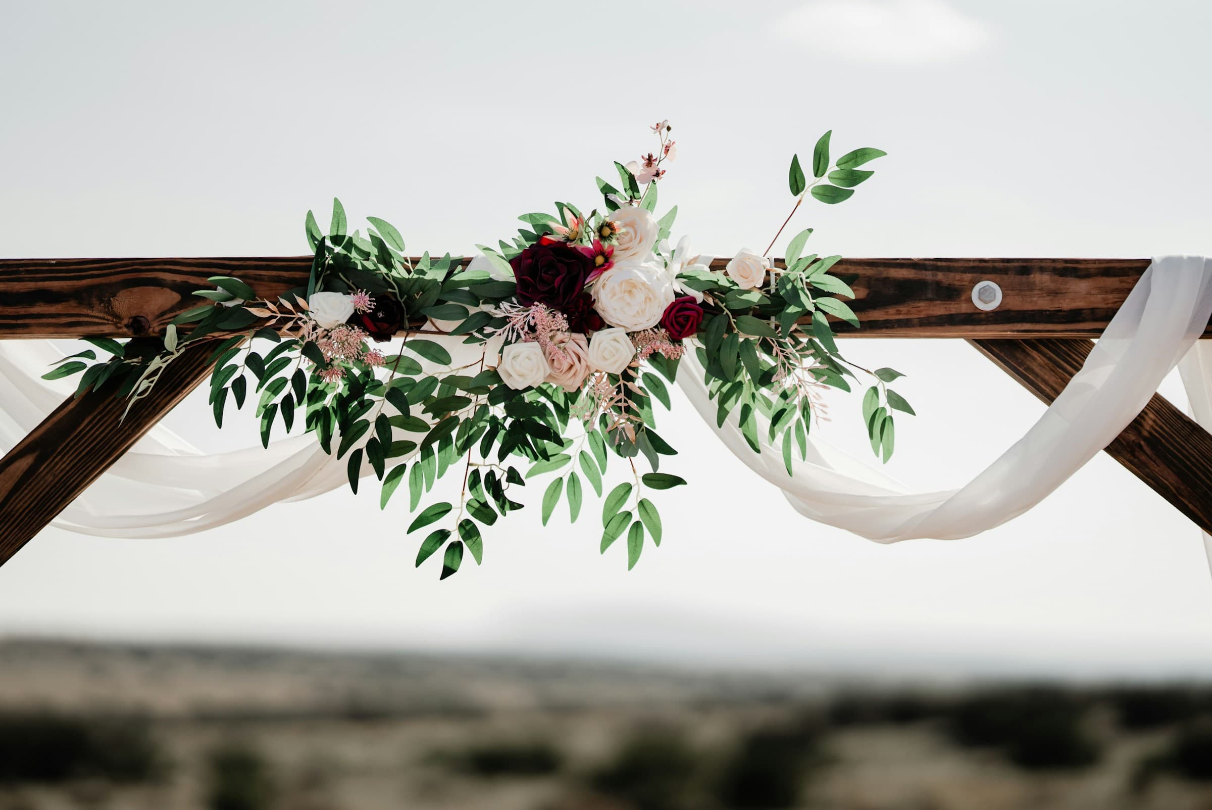 An outdoor wedding arch decorated with flowers and trailing greenery